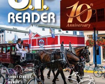 UPPAA Cover of U.P. Reader 10th Anniversary edition featuring a street scene with two horses pulling a carriage, cyclists passing by, and colorful buildings in the background. Text highlights magazine contents and the Upper Michigan focus.