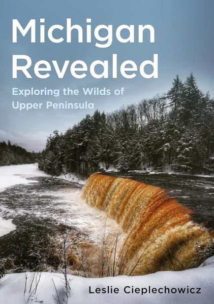 UPPAA Book cover for “Michigan Revealed: Exploring the Wilds of Upper Peninsula” by Leslie Cieplechowicz, featuring a winter scene of a river and waterfall with snow-covered trees in the background.