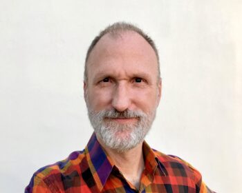UPPAA A middle-aged man with a gray beard wearing a multicolored plaid shirt.
